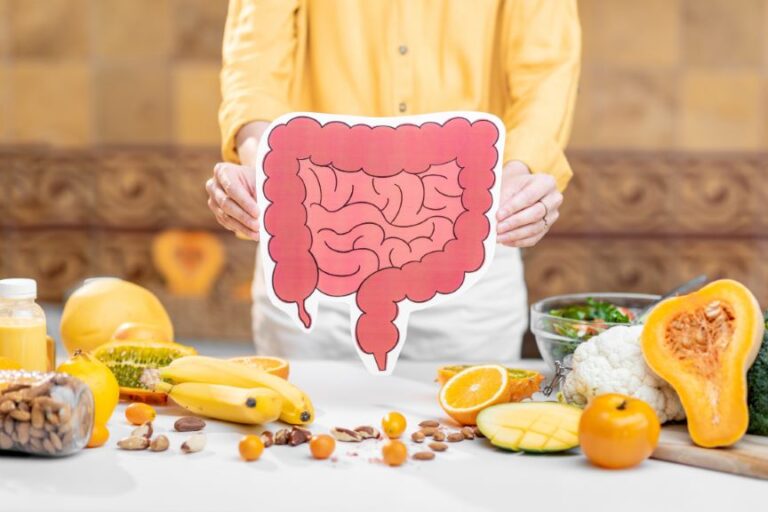 A person holding a pink intestine cutout over a table filled with oranges, broccoli, squash, and nuts.